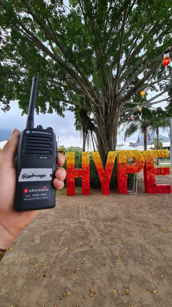 Imagem de rádio da Gávea Rádios, cliente da Fizzing, nas mãos de um profissional trabalhando no festival Babilônia Hype 